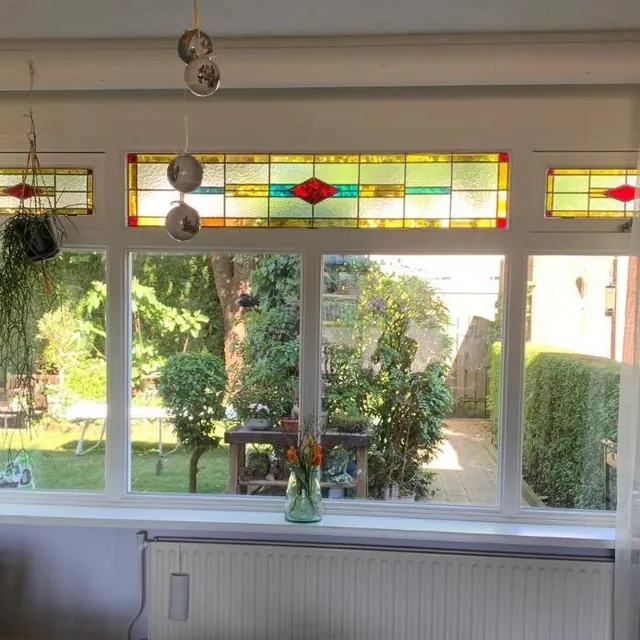 Rij bovenlichten met rode, gele en groene ruitjes boven een raam met tuinzicht