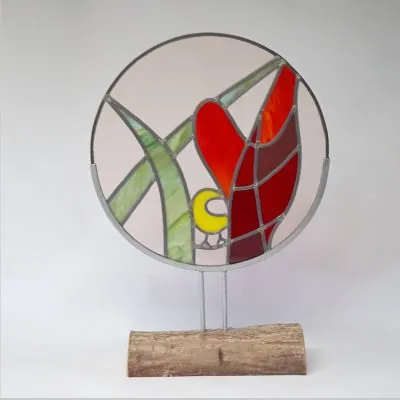 Rond glas-in-loodwerk met een gele vogel en rode tulp op een houten voet