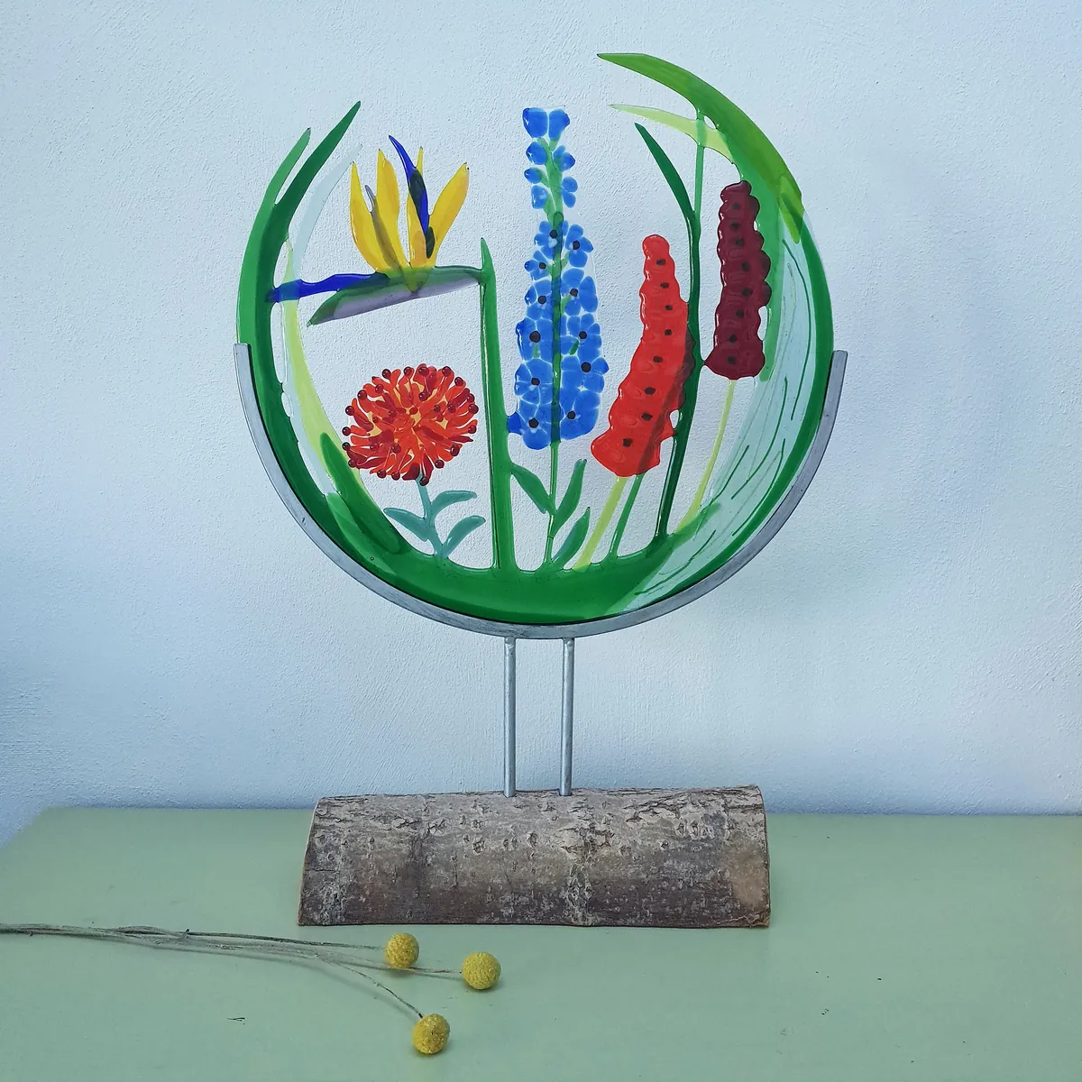 Ronde glasfusing van een veldboeket met oranje, blauwe en rode bloemen op een standaard