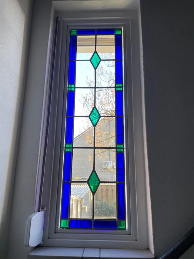 Smal zijraam bij de trap met diepblauw glas in lood en groene ruiten